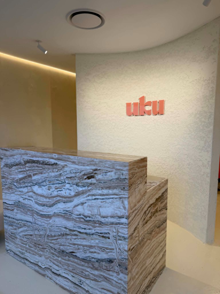 UKU reception desk and coral logo on a textured wall at the Southport studio